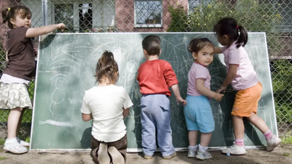Fünf Kinder in einer Kita im Garten malen an einer Tafel.