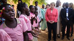 Bundeskanzlerin Angela Merkel wird beim Besuch einer Schule singend begrüßt.