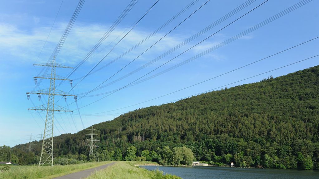 Stromleitungen vor blauem Himmel an einem Fluss