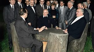 Bundeskanzler Helmut Kohl ( r.) im Gespräch mit Michael Gorbatschow, Präsident der UdSSR (M.) und Hans-Dietrich Genscher, Bundesminister des Auswärtigen, an einem Holztisch.