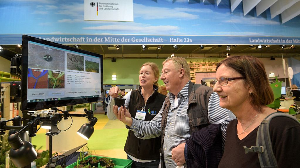 Zwei Frauen und ein Mann stehen vor einem Monitor auf der Internationalen Grünen Woche in Berlin.