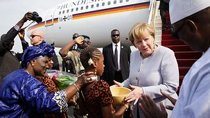Bundeskanzlerin Angela Merkel wird auf dem Flughafen in Bamako von Mädchen mit Blumen und Wasser-Kalebassen begrüßt.