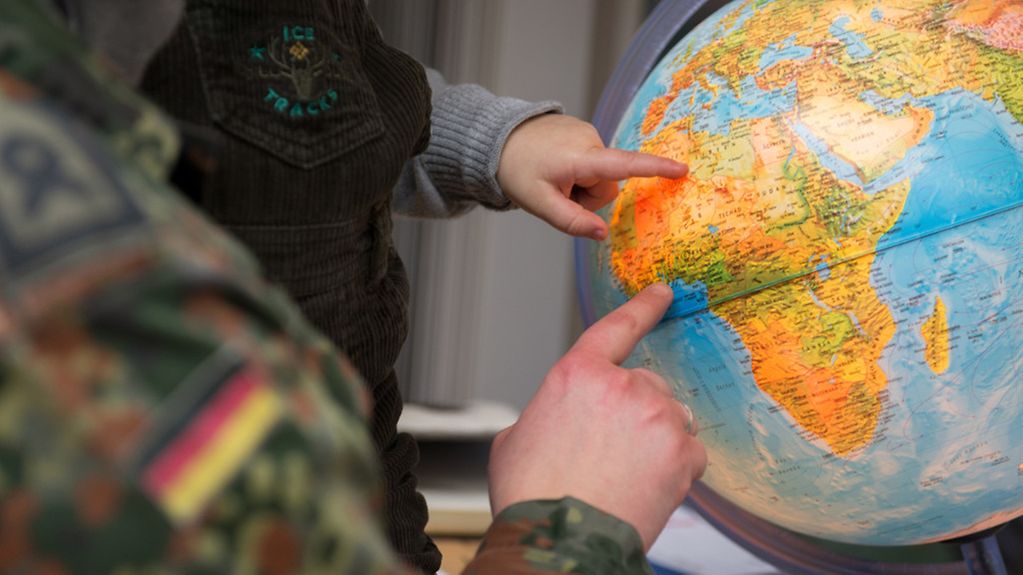 A soldier and a child look at a globe together.