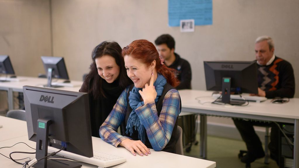 Zwei Frauen blicken gemeinsam auf Bildschirm eines Computers.
