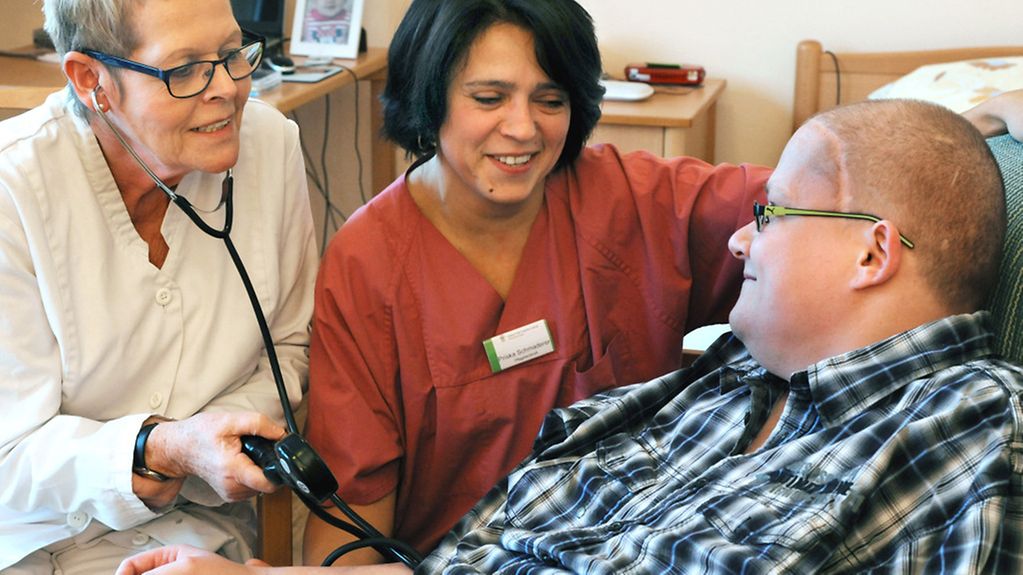In einem Hospiz sprechen eine Palliativmedizinerin und eine Palliativschwester mit einem Todkranken.