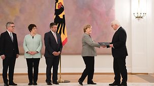 Federal President Frank-Walter Steinmeier presents Chancellor Angela Merkel with her certificate of discharge.
