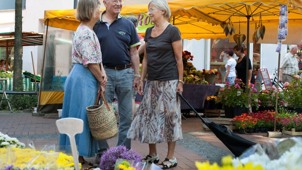 Drei Rentner im Gespräch auf einem Wochenmarkt.