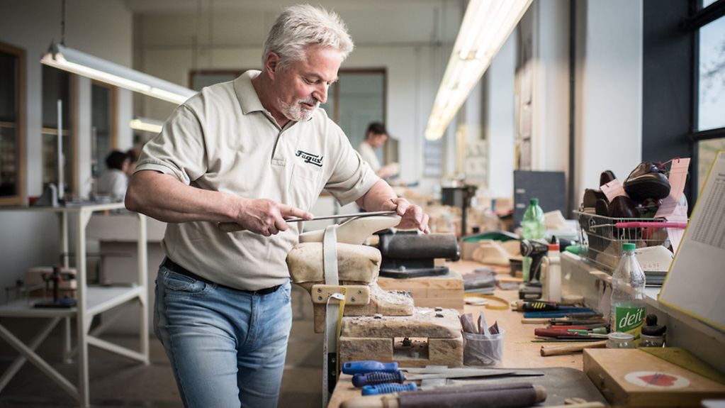 Ein älterer Mitarbeiter in der Modellabteilung 'Entwicklung' einer Firma, die traditionell Schuhleisten herstellt.