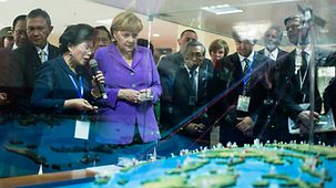 An einem Modell lässt sich Merkel die Funktionsweise des Frühwarnsystems erklären.