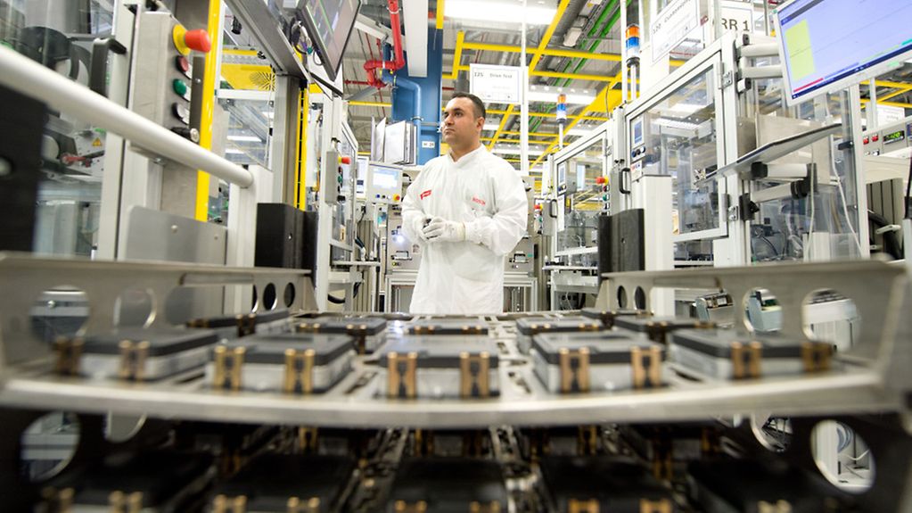 A skilled worker standing in front of a batch of radar sensors destined for the automotive industry