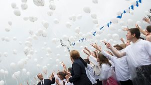 Bundeskanzlerin Angela Merkel und Frankreichs Präsident François Hollande lassen mit Kindern Luftballons steigen.