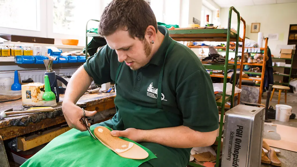 Ein Schuster der Orthopädie Schuhtechnik in Schwarzenberg schneidet Material für eine Sohle zu.