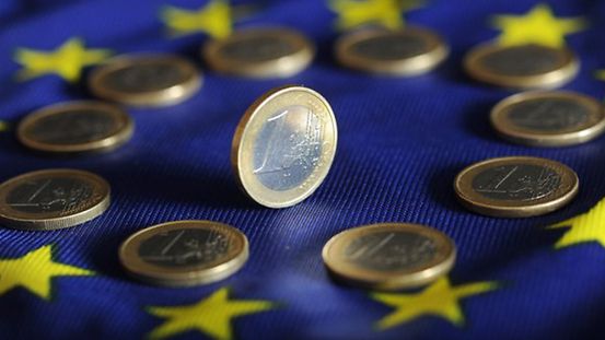 Auf einer Europafahne liegen mehrere Ein-Euromünzen