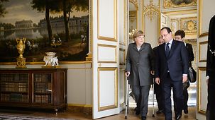 Federal Chancellor Angela Merkel and French President François Hollande walk side by side inside Élysee Palace.