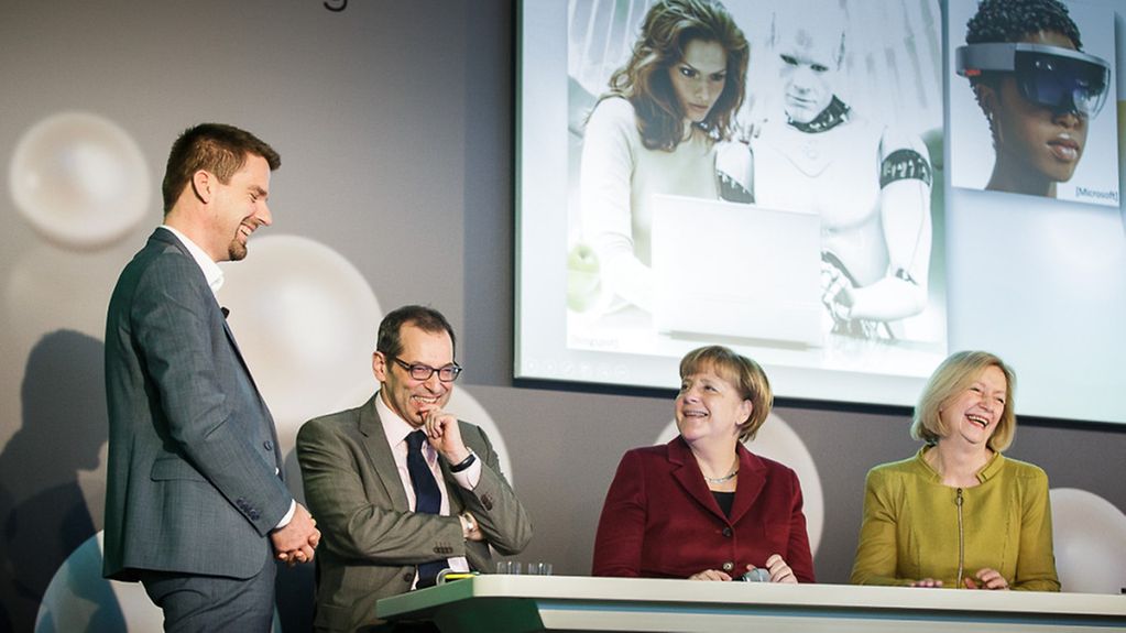 Kanzlerin Angela Merkel und Bundesministerin Johanna Wanka (rechts) sitzen an einem Tisch bei der Präsentation von 10 Forschungsobjekten der Max-Planck-Gesellschaft und der Fraunhofer-Gesellschaft
