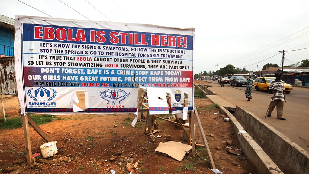 Des habitants de Paynesville, au Libéria, passent devant une affiche mettant en garde contre l'Ebola