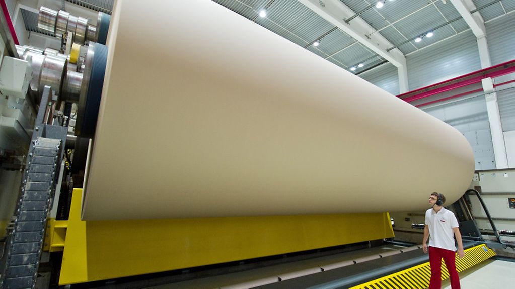 In einer Papierfabrik: ein Mitarbeiter vor einer riesigen Rolle mit Wellpapperohpapier