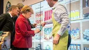 Merkel mit Smartphone an der digitalen Verkaufswand.