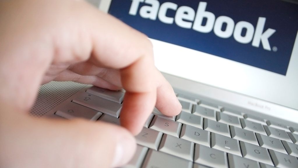 Hand auf Tastatur eines Laptops, dessen Bildschirm "Facebook" anzeigt