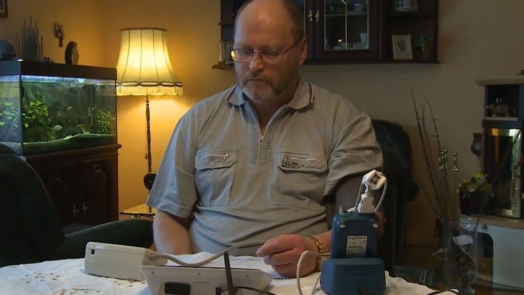 Mann sitzt mit Blutdruckmessgerät an einem Tisch.