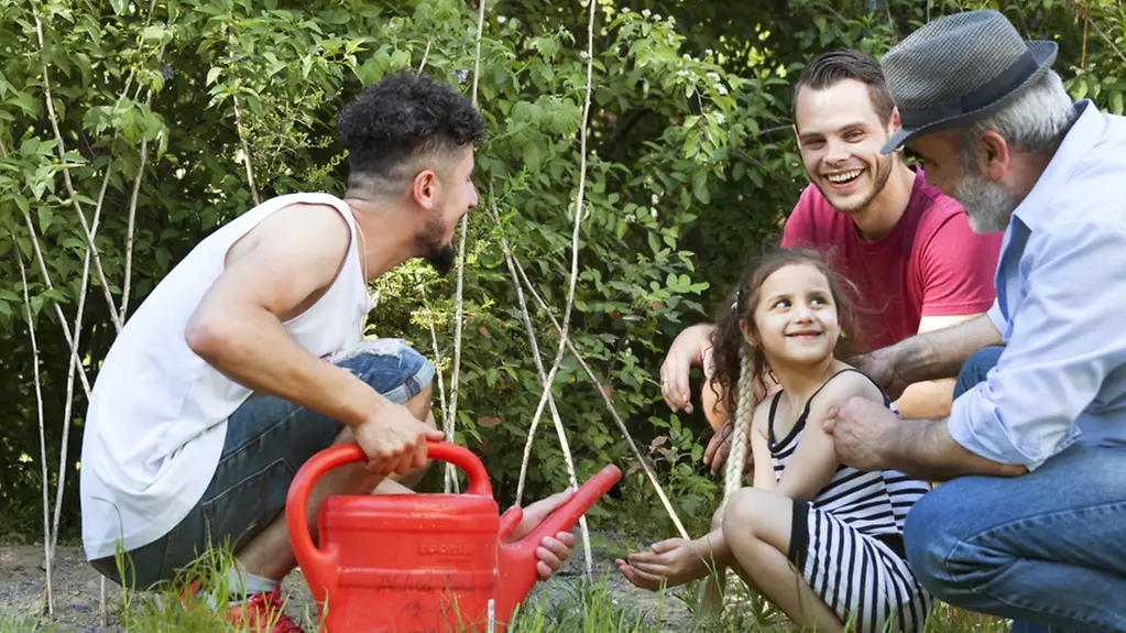 Geflüchtete mit einem Erzieher bei gemeinsamen Gartenarbeiten im Gartenprojekt "Garten der Hoffnung" in Berlin