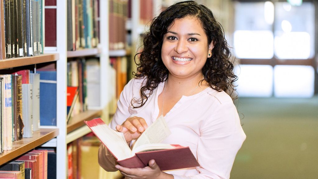 Die mexikanische Studentin Rosalia Meztli Chino Flores steht in der Bibliothek der Universität Köln mit einem Buch in der Hand.