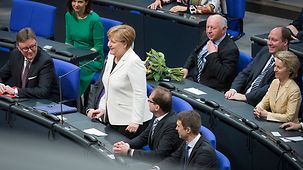 Angela Merkel steht im Bundestag neben Abgeordneten an der Regierungsbank und nimmt Wiederwahl als Bundeskanzlerin an.