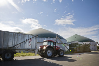 Ein Traktorgespann mit Anhänger fährt an einer Anlage zur Biogasgewinnung vorbei.