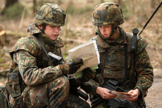 Zwei Bundeswehrsoldaten im Kampfanzug orientieren sich anhand von Karten im Gelände. 