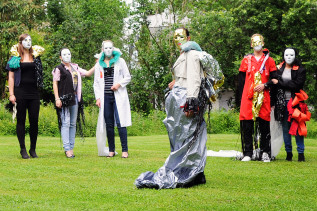 Ein Theatergruppe probt im Park. Alle sechs Personen tragen Masken und Kostüme.