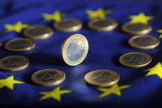 Ein-Euro-Münzen liegen kreisförmig auf der Europa-Flagge, in der Mitte steht eine weitere Münze