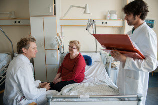 Zwei Ärzte betreuen eine ältere Patientin am Krankenbett einer Klinik.