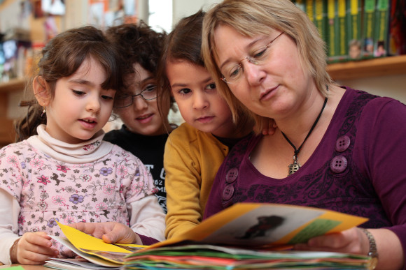 Eine Kindergärtnerin liest Kindern aus einem Buch vor